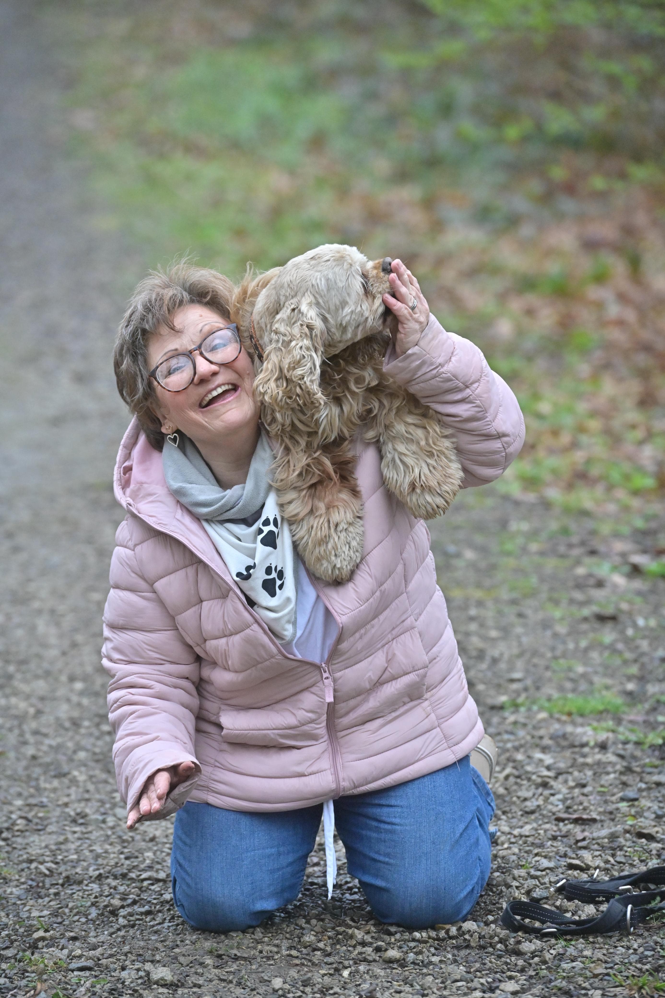 Jutta Gaßmann kniet lachend auf einem Waldweg, während einer ihrer Cocker Spaniel sich an sie schmiegt